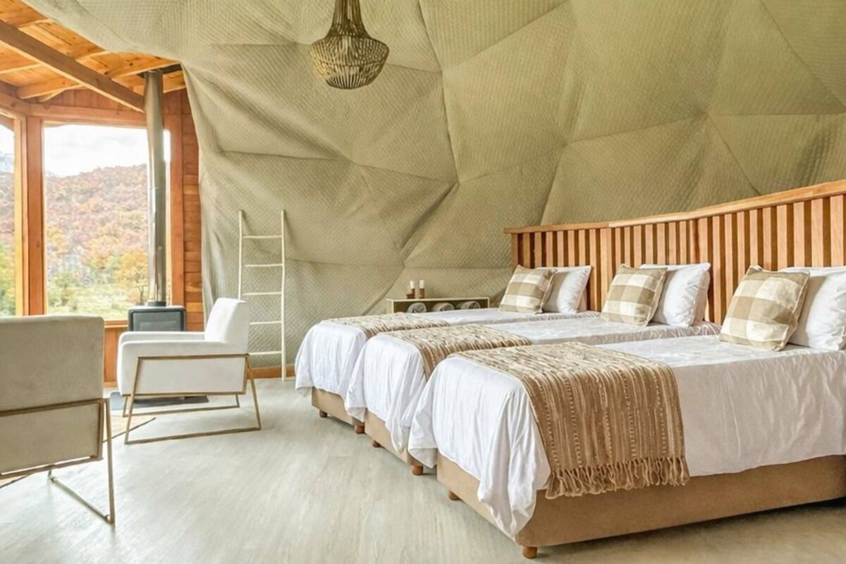 A spacious bedroom with a high ceiling, wooden headboard, and a large window offering a view of the outdoors.