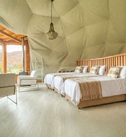 A spacious bedroom with a high ceiling, wooden headboard, and a large window offering a view of the outdoors.