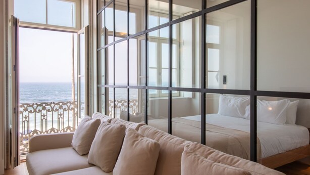 A room with a bed, a sofa, and a view of the ocean. - Luz 147 | Seaside Oasis by LovelyStay (Porto)