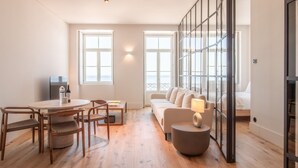 A modern living room with a sofa, a round table with chairs, and a TV. - Luz 147 | Seaside Oasis by LovelyStay (Porto)