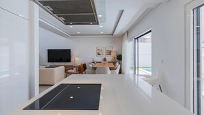 A modern living room with a flat-screen TV, a dining area with a table and chairs, and a large window offering a view of the outdoors. - Villa Aroeira w/ Pool by LovelyStay (Aroeira)