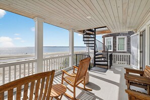 A covered balcony with wooden chairs, a spiral staircase, and a view of the beach. - Beachfront 3 Bed, 3.5 Bath - Unobstructed Ocean Views (St. Simons Island)