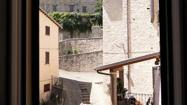 Uma rua estreita com edifícios de pedra, uma escadaria e vista para um prédio maior com uma torre.