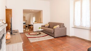 Uma sala de estar com sofá, televisão, lareira e cozinha ao fundo.