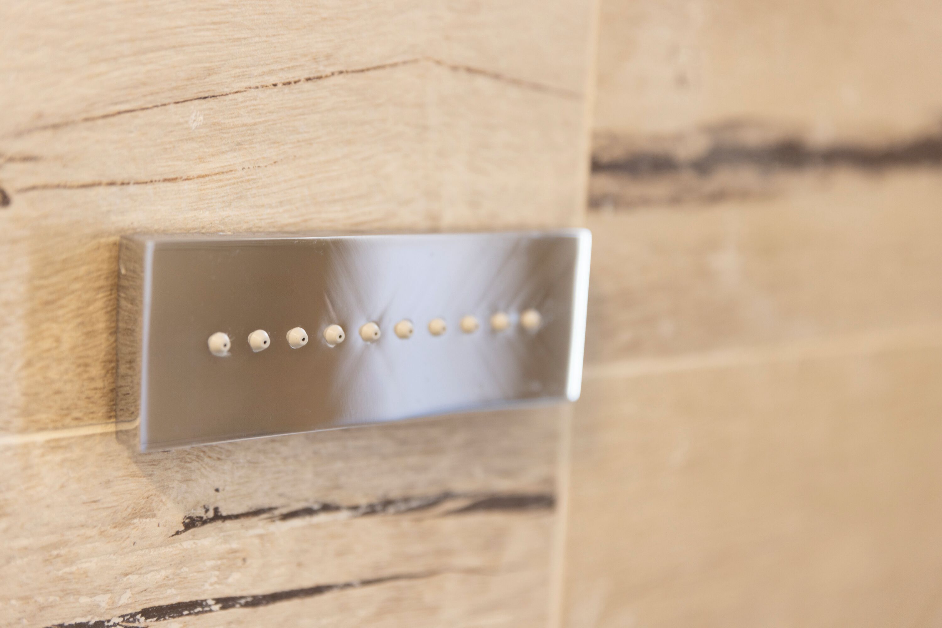 Un objeto metálico y rectangular con seis elementos sobresalientes, montado sobre una superficie de madera con veta y textura visible.