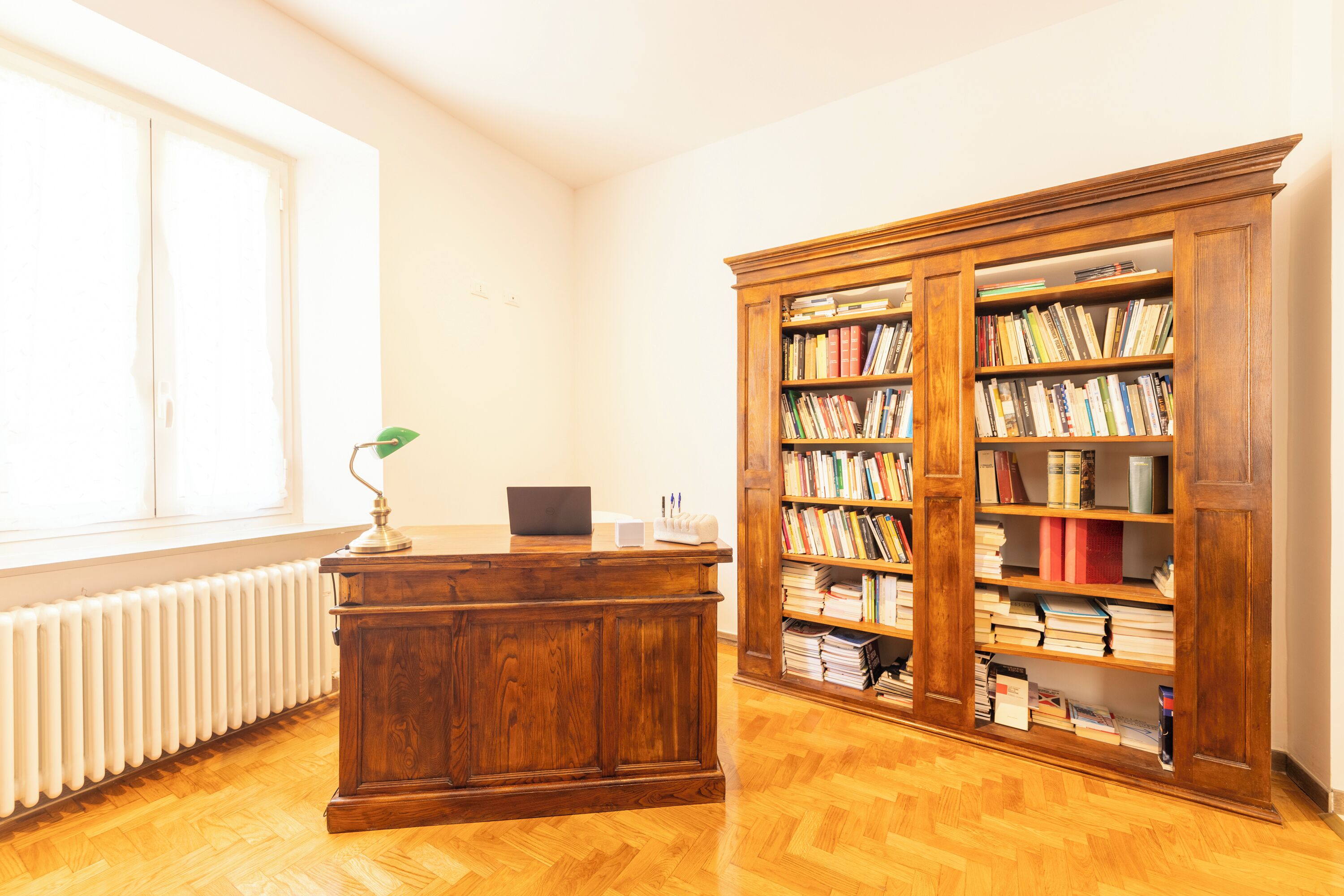 A room with a wooden desk, a bookshelf, and a window.