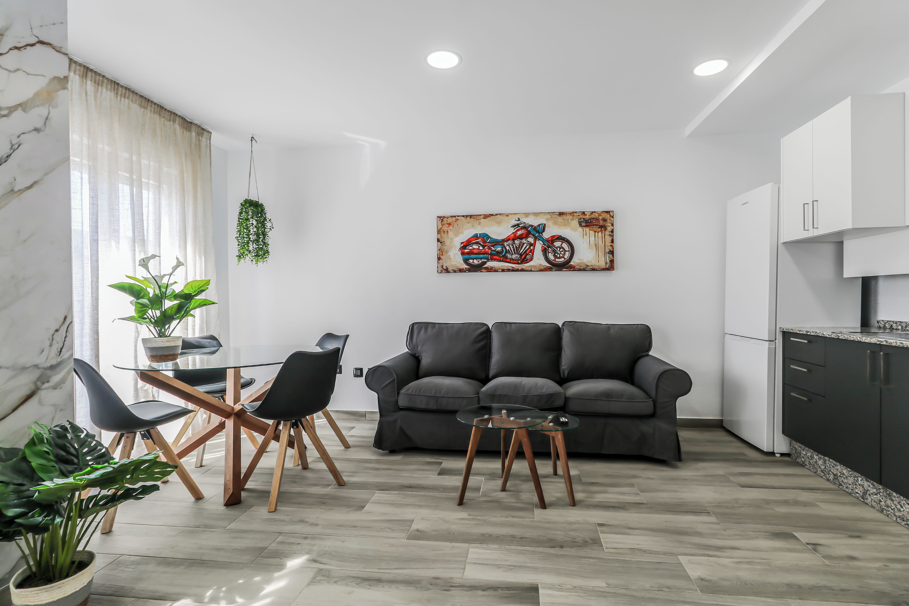 Un saló modern amb un sofà, una taula de centre i una zona menjador amb cadires. Hi ha un quadre d'una moto a la paret.