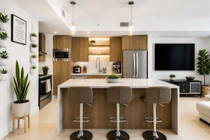 Une cuisine moderne avec un îlot central, des tabourets de bar, un téléviseur et des plantes en pot.
