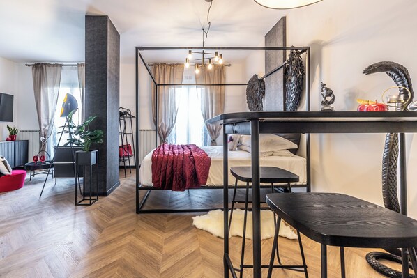 Un salon moderne avec un parquet en chevrons, un canapé rouge, un meuble TV en métal noir et un coin repas avec une table et des chaises noires.