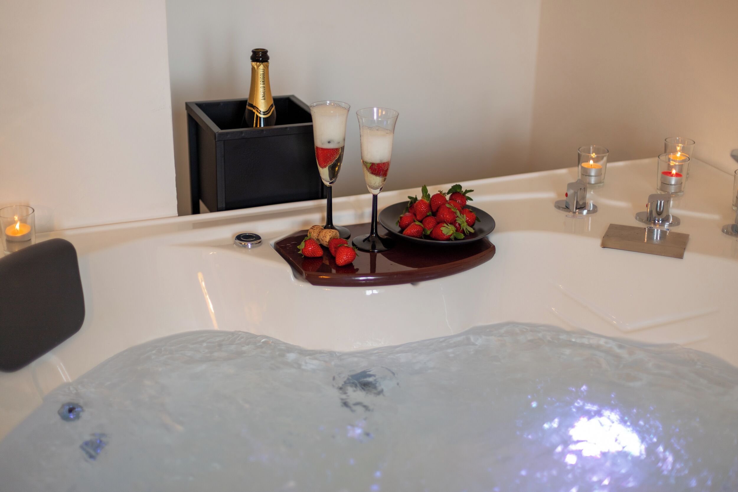 Un'area spa con vasca idromassaggio, flute di champagne, fragole e candele.