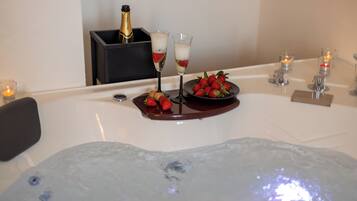 Un'area spa con vasca idromassaggio, flute di champagne, fragole e candele.