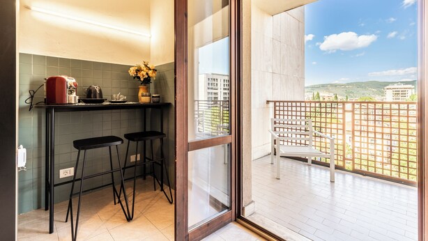 A kitchen with a bar area, two stools, and a view of a balcony with a wooden fence and a bench. - Luxury Suite - Tentazioni Romantiche (Perugia)