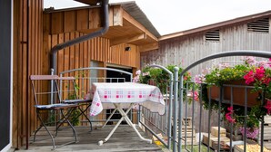 Une terrasse en bois avec une table et des chaises, une rambarde en métal et un bâtiment en bois en arrière-plan.