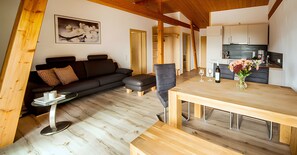 Een moderne woonruimte met een houten vloer, een bank, een eettafel en een keukenhoek.