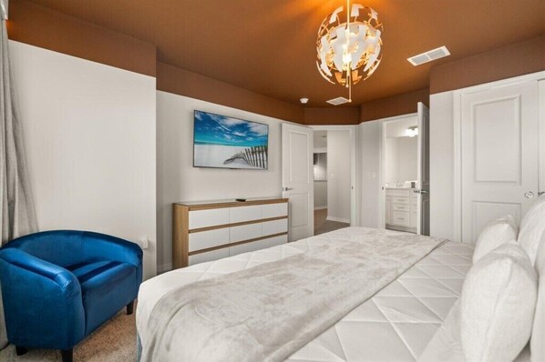 A bedroom with a large bed, a blue chair, a dresser, and a painting on the wall.