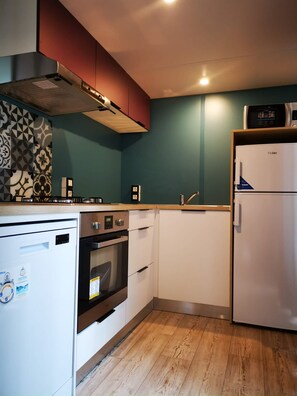 A compact kitchen with white cabinets, a built-in oven, a dishwasher, and a refrigerator.