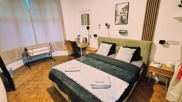 Een hotelkamer met een bed, een bureau, een stoel, een klein tafeltje, een nachtkastje en een raam met gordijnen.