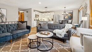 A modern living room with a grey sofa, a coffee table, and a dining area with a chandelier.