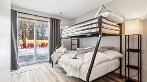 A bunk bed room with a view of a snowy outdoor area, a sliding glass door, and a bedside table with a lamp.