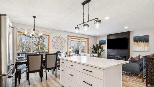 A modern kitchen with a central island, dining area with chairs, and a living area with a sofa and TV.