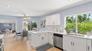 Een moderne keuken met witte kasten, een vaatwasser en een groot raam met uitzicht op groen.