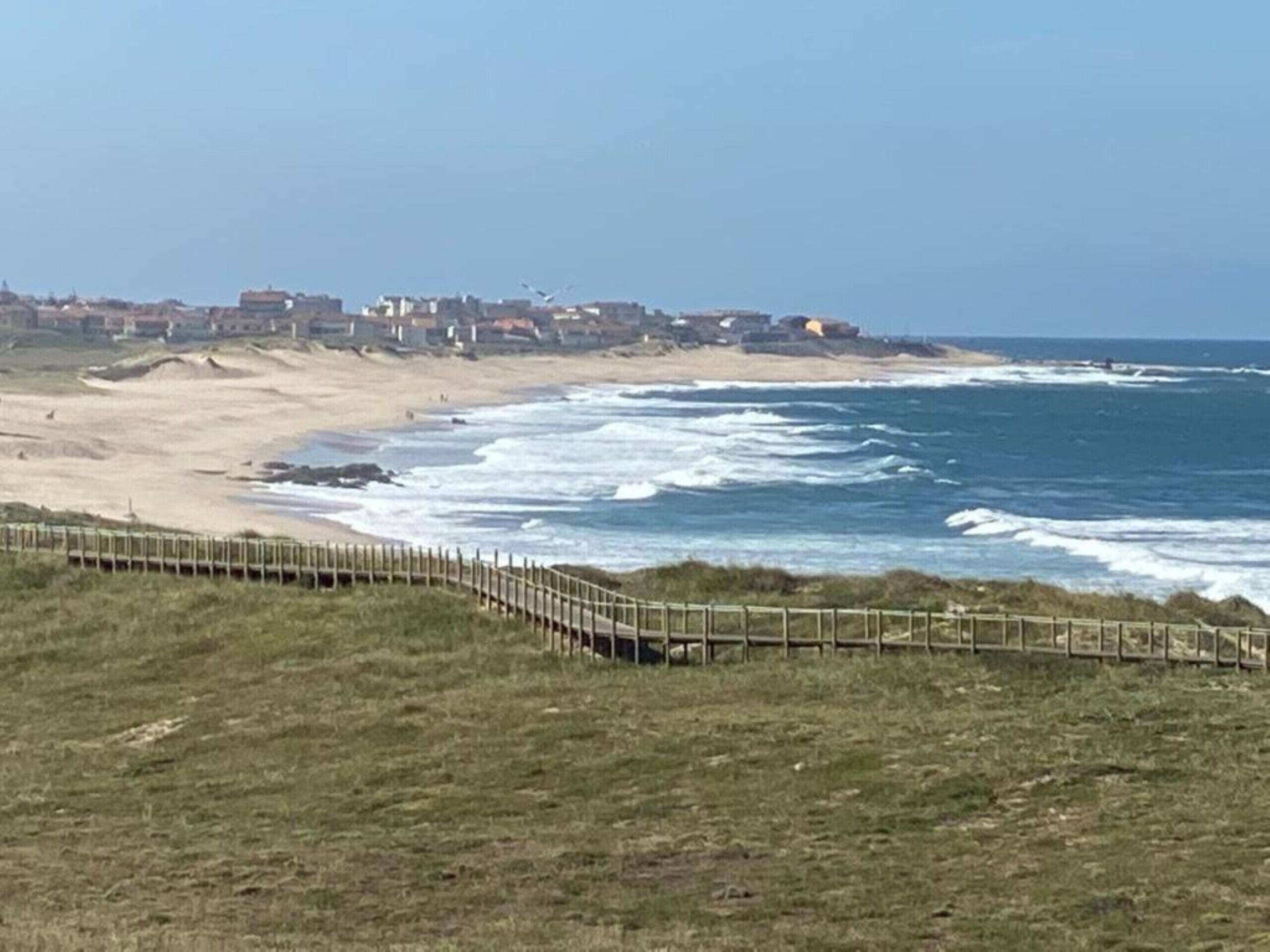 Paisagem costeira com uma praia arenosa, ondas e uma cerca de madeira.