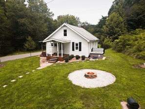 Een wit huis met één verdieping, met een veranda, een jacuzzi en een vuurkorf in de tuin.