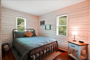 Une chambre à coucher avec un lit, une table de chevet, une lampe et deux fenêtres.