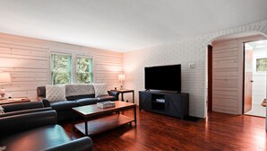 A modern living room with a sofa, coffee table, TV, and wooden flooring. - Shorty's Place | Hocking Hills, 80 Acres, Hot Tub (South Bloomingville)
