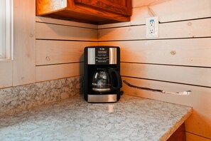 Une machine à café posée sur un plan de travail de cuisine, avec un revêtement mural en bois et un pare-feu en marbre.
