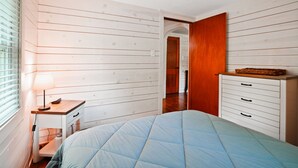 Una camera da letto con un letto, un comodino, una cassettiera e una porta che dà su un'altra stanza.