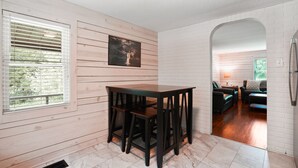 Una stanza con parete in legno, un tavolo scuro in legno con sedie, una finestra con persiane e un muro in mattoni bianchi.