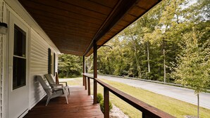 Un portico in legno con due sedie, una panchina e vista su una strada e alberi.