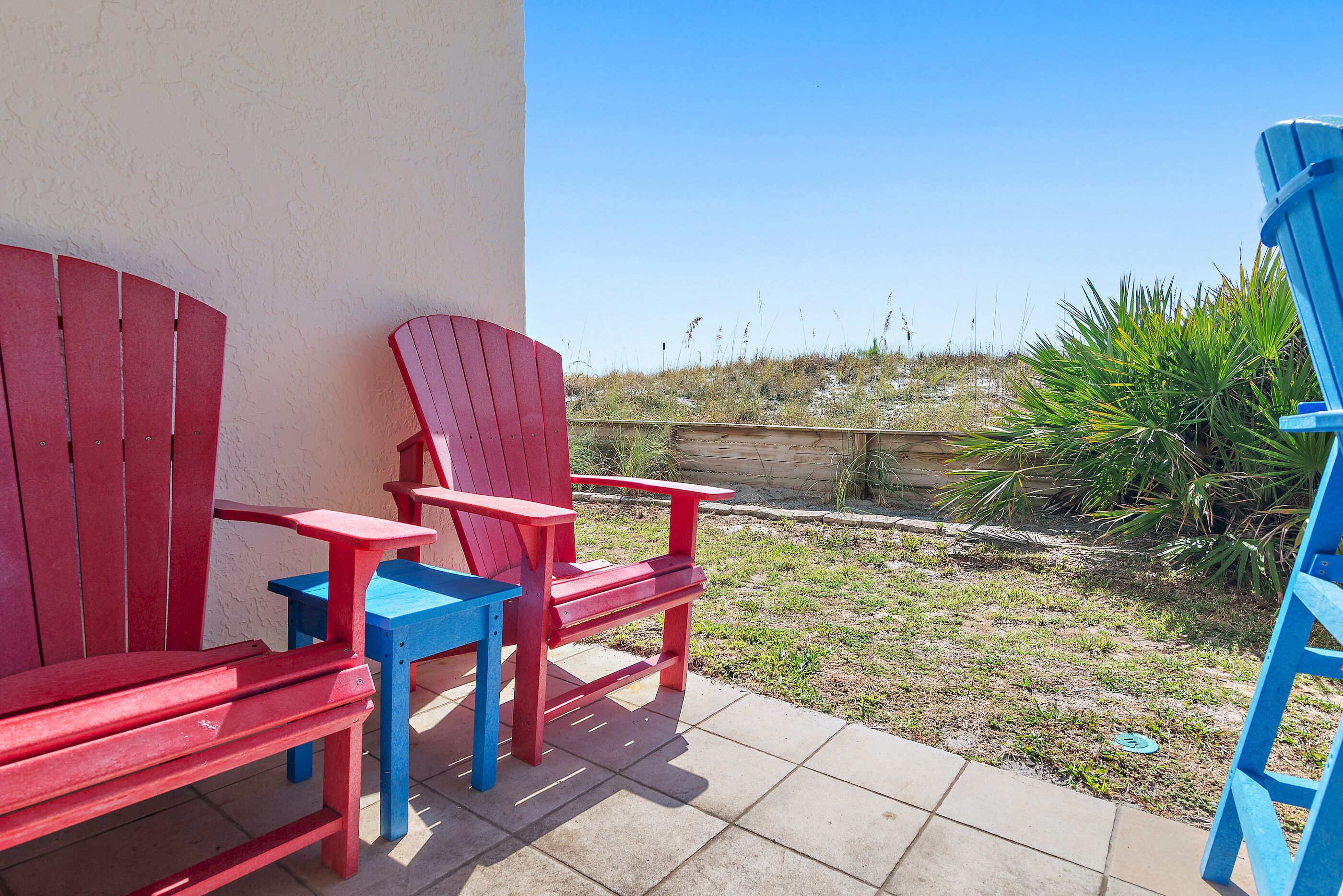 Une terrasse avec des chaises Adirondack rouges et bleues et un sol en béton.