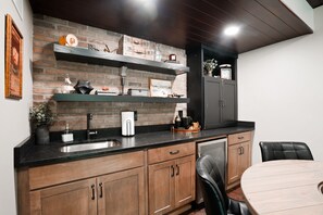 Une cuisine avec un mur en briques, des armoires en bois, un plan de travail noir et un coin repas comprenant une table ronde et des chaises noires.