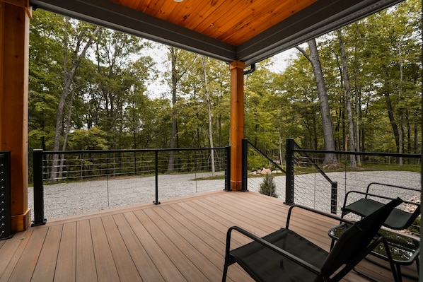 A wooden deck with a railing, chairs, and a view of a forest.