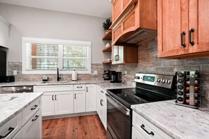 A kitchen with white cabinets, a stainless steel stove, a coffee maker, and a wine rack. - On The Rocks | Hocking Hills, 4BR, Hot Tub (South Bloomingville)