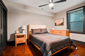 Een slaapkamer met een bed, nachtkastjes, een plafondventilator, een raam met jaloezieën en een schilderij aan de muur.