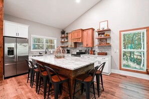A modern kitchen with a large island, bar stools, stainless steel appliances, and wooden cabinetry. - On The Rocks | Hocking Hills, 4BR, Hot Tub (South Bloomingville)