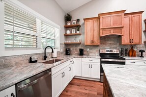 Een moderne keuken met witte kasten, een granieten aanrechtblad, een ingebouwde oven en een backsplash van baksteen.