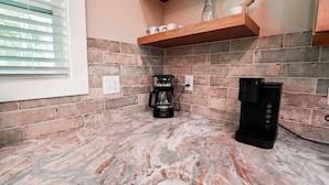 A kitchen with a coffee maker, a water dispenser, and a brick backsplash. - On The Rocks | Hocking Hills, 4BR, Hot Tub (South Bloomingville)