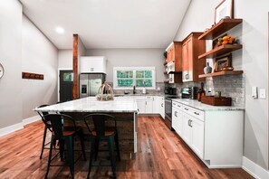 A modern kitchen with white cabinets, a marble island, and a wooden floor. - On The Rocks | Hocking Hills, 4BR, Hot Tub (South Bloomingville)