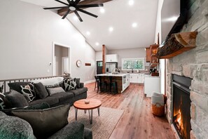 Een moderne woonkamer met een open haard, een keuken met witte kasten en een eethoek met een ronde tafel.