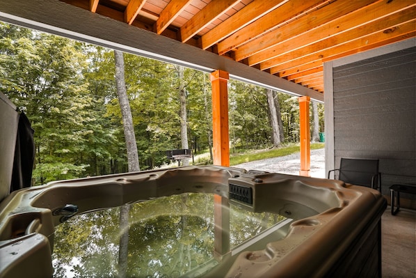 Un bain à remous avec vue sur une forêt, des poutres en bois au plafond et un fauteuil.