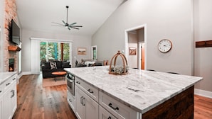 A modern kitchen with a large island, white cabinetry, and a stone fireplace. - On The Rocks | Hocking Hills, 4BR, Hot Tub (South Bloomingville)