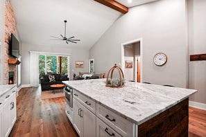 A modern kitchen with a large island, white cabinetry, and a stone fireplace. - On The Rocks | Hocking Hills, 4BR, Hot Tub (South Bloomingville)