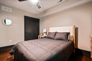 Une chambre à coucher avec un lit, une table de chevet, une lampe, une porte et un miroir fixé au mur.