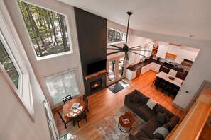 A modern kitchen with a dining area, a fireplace, and large windows overlooking a forest.