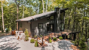 A modern cabin with a deck, surrounded by trees.