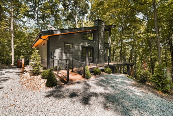 A modern cabin with a deck, surrounded by trees.